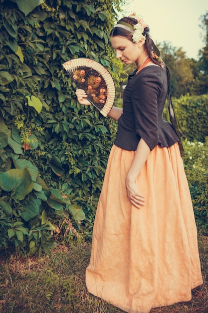Портрет женщины брюнетки, одетой в историческую одежду в стиле барокко со старой модной прической, на открытом воздухе. Средневековое платье среднего класса