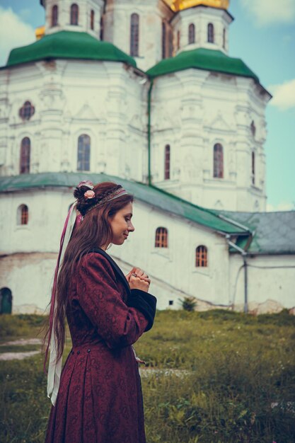 야외에서 역사적인 바로크 옷을 입고 기도하는 갈색 머리 여자의 초상화