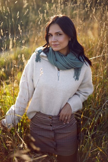 Portrait of a brunette woman in a sweater and scarf in autumn in a field