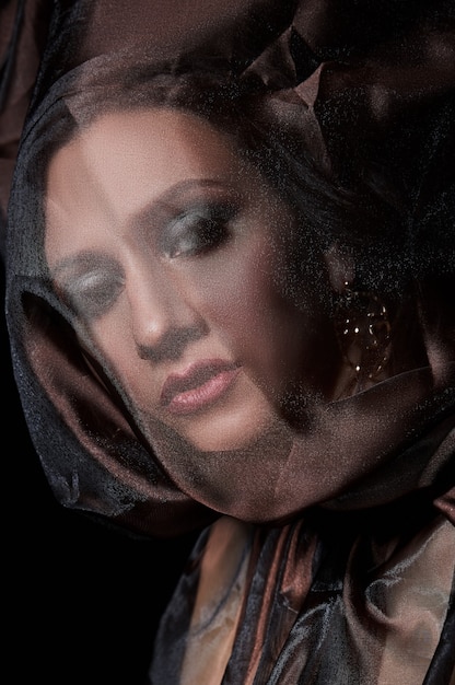 Portrait of a brunette woman through a transparent dark fabric. Beauty and makeup girl. There is no focus