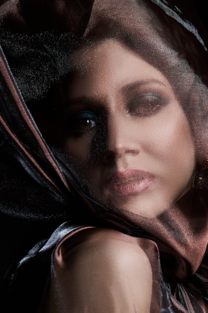 Portrait of a brunette woman through a transparent dark fabric.