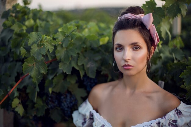 Foto ritratto di donna bruna in un abito bianco si trova in un vigneto in estate in italia