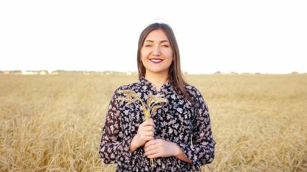 Portrait of a brunette woman with a bouquet of ears of ripe wheat in a field