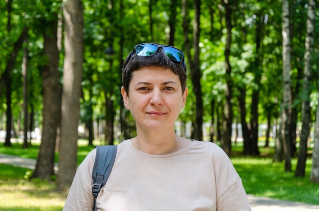 Portrait of brunette woman woman stands on the background of trees in a city park