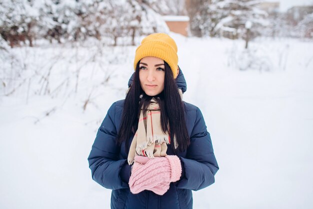 Photo portrait of a brunette woman in a yellow hat on a background of a winter forest