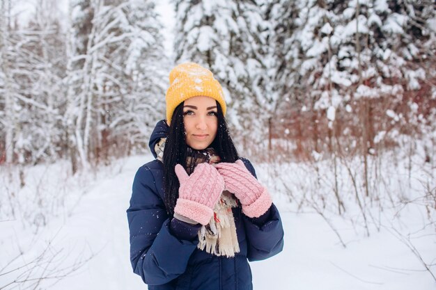 Portrait of a brunette woman in a yellow hat on a background of a winter forest