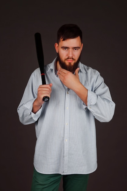Portrait of brutal, bearded, aggressive, big person with baseball bat in hand on dark background. Angry human bodyguard with stern look. Mafia man is ready to protect against violence and underground
