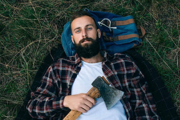 Photo portrait brutal bearded and moustached woodcutter hipster gypsy man in the forest with ax man lying on the grass and dreamsx9