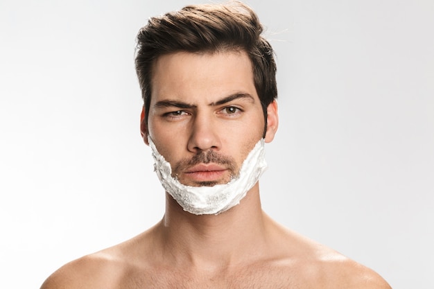 Portrait of brutal half-naked man with shaving foam on his face isolated on white