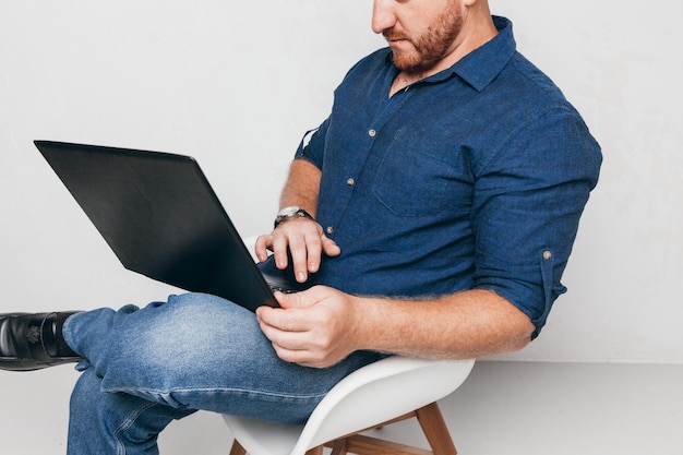 Portrait of a brutal man sitting on a chair against a white wall with a laptop and notepada business man