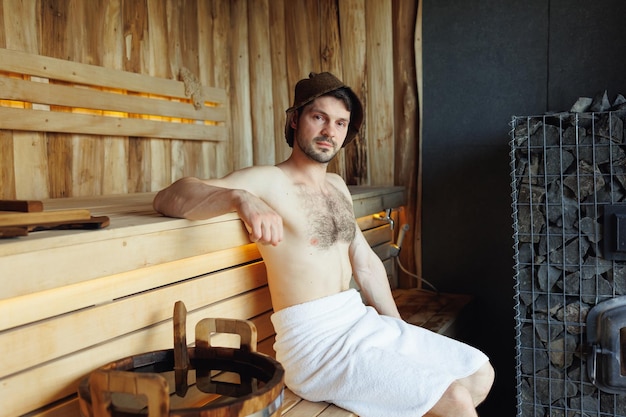 Portrait of a brutal man sitting on a wooden bench in a Finnish sauna