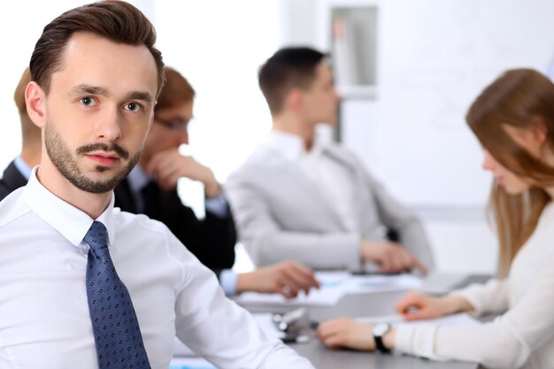 Portrait of business man  against a group of business people at a meeting.