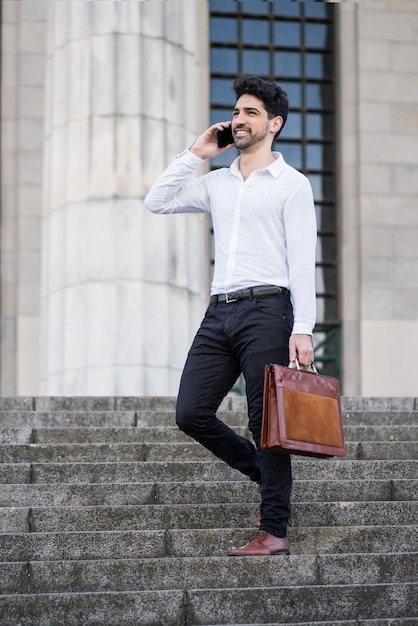 Portrait of business man talking on the phone while standing on stairs outdoors.