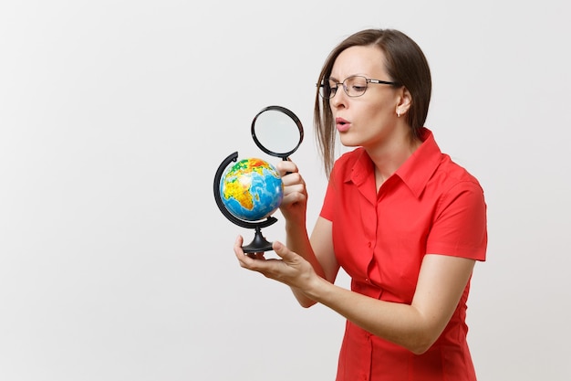 Portrait of business teacher woman in red shirt holding and looking through magnifying glass on globe isolated on white background. Education teaching in high school university concept. Copy space.