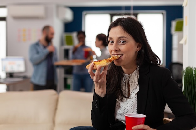 Portrait of business woman celebrating with drinks after work, meeting with colleagues in startup office. Young adult enjoying pizza and beer beverage at fun party celebration.