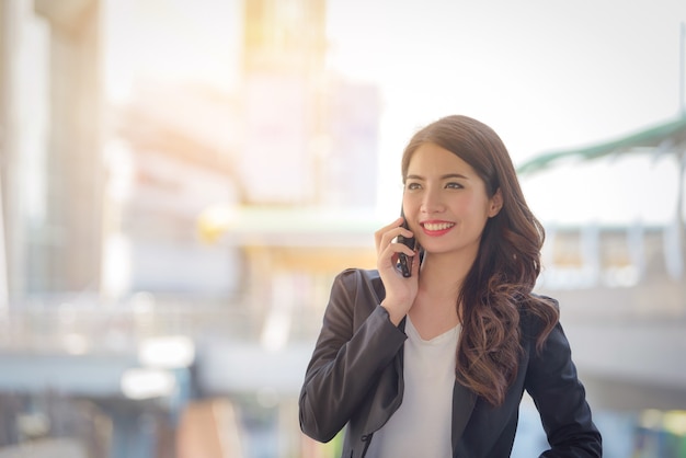 ビジネスの女性の幸せ笑顔スマートフォンで話すぼかしの背景の肖像画。