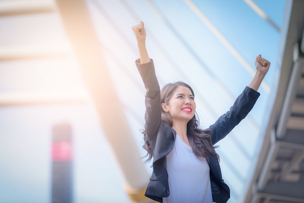 Portrait of business woman smiling with arms up celebrate on blurred city