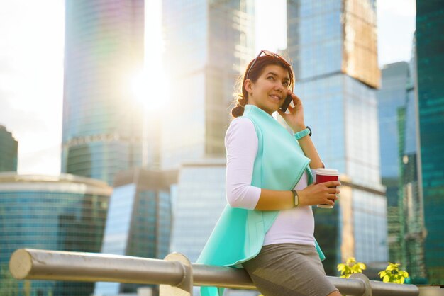 Photo portrait of business woman walking and smiling outdoor with laptop and cup of coffee