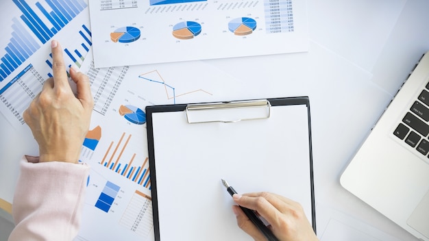 Portrait of business woman with laptop, finance graph and writes on a document at her office