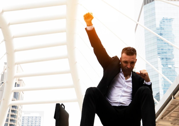 Photo portrait of businessman clenching fist while sitting on steps in city