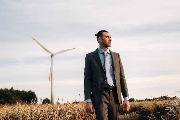 Portrait of a businessman in a gray suit on a wheat field against the background of a windmill and the evening sky