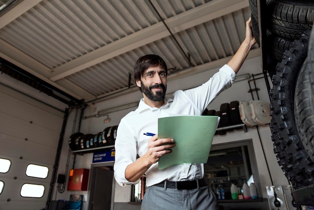 Portrait of businessman holding document while standing with tires in garage