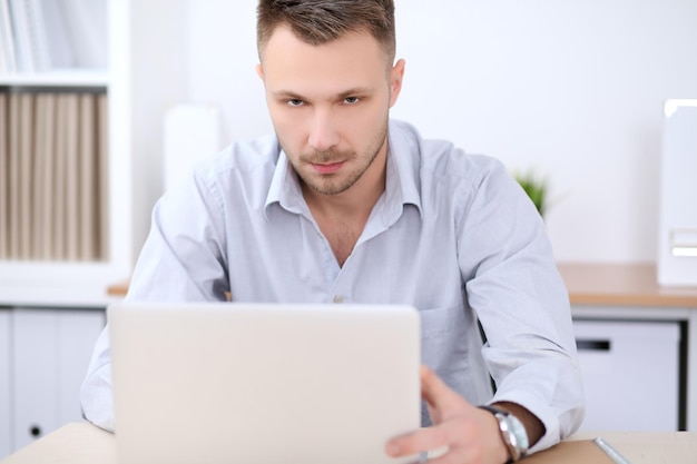 Portrait of businessman sitting at the desk in office workplace.