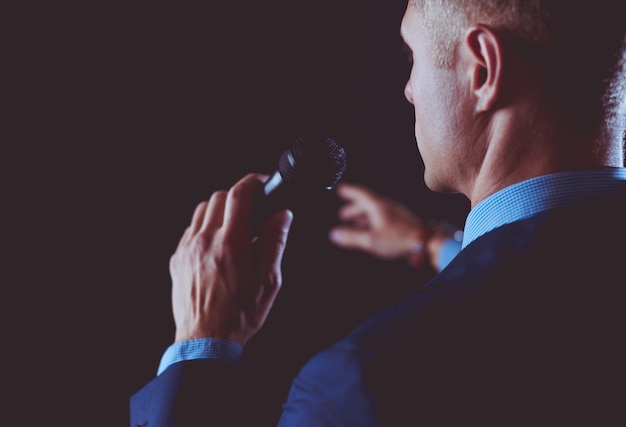 Портрет бизнесмена, стоящего с микрофоном и смотрящего вперед, выступает на конференции