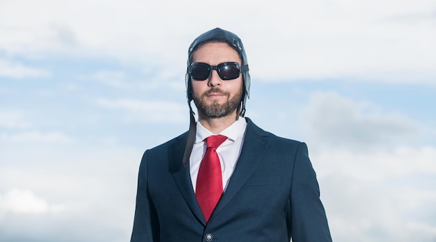 Portrait of businessman in suit and pilot hat on sky background