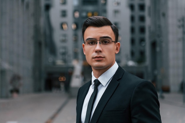 Portrait of businessman that is in black suit and tie is outdoors in the city