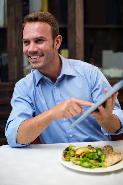 Foto ritratto dell'uomo d'affari che per mezzo della compressa digitale mentre mangiando alimento