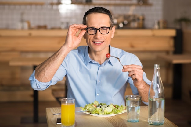 カフェで新鮮なサラダを食べてカメラを見ている眼鏡をかけているビジネスマンの肖像画
