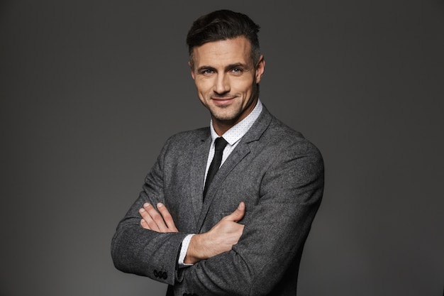 Portrait of businessman wearing formal costume standing with arms folded and smiling , isolated over gray wall