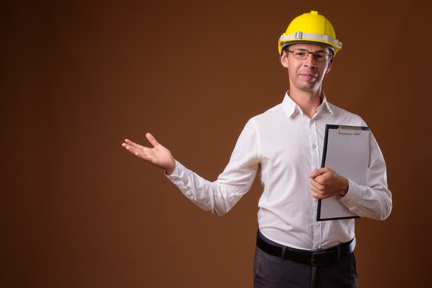 Portrait of businessman wearing hardhat against brown wall