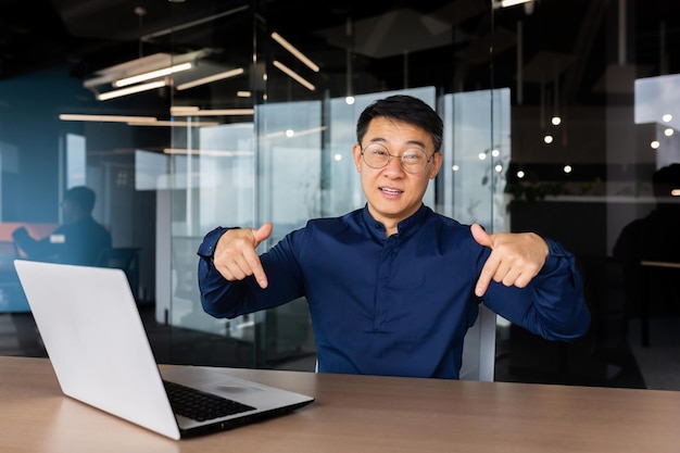 Portrait of businessman with laptop inside office man smiling and looking at camera pointing with