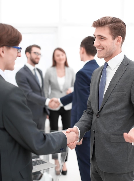 Portrait of businessmen shaking hands with colleagues on background