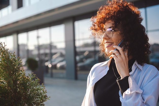 Portrait of a businesswoman having phone conversations woman with curly hair and glasses smiling con...