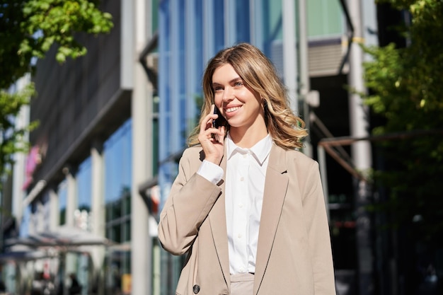 Portrait of businesswoman making a phone call standing on\
street near office building talking to som