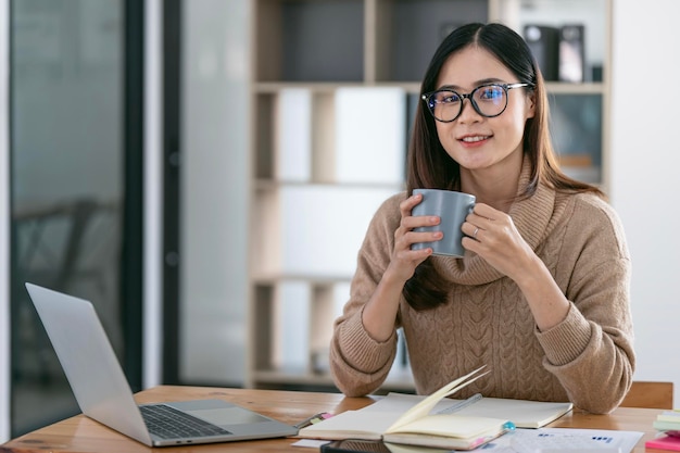 Portrait of businesswoman sitting at desk holdilng mug and looking with confidence at camera