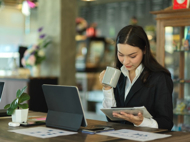 Portrait of businesswoman take a coffee break while reading paperwork in cafe