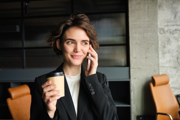 携帯電話で話す実業家のポートレートがオフィスに立ち、コーヒーを飲む