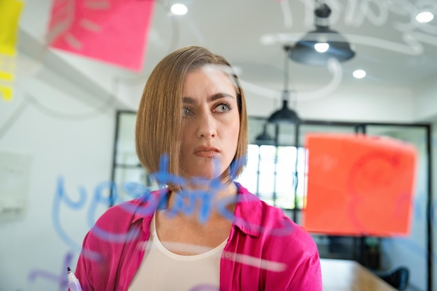 Portrait of businesswoman thinking while standing in front of board immaculate