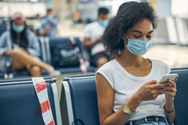 Ritratto di donna d'affari che indossa una maschera facciale durante l'epidemia di virus mentre è seduta nella sala partenze dell'aeroporto