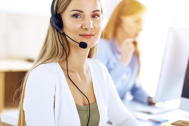 Portrait of call center operator at work in sunny office. Group of people in a headset ready to help customers. Business concept.