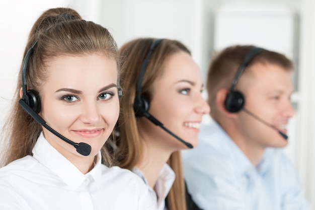 Portrait of call center worker accompanied by her team. Smiling customer support operator at work. Help and support concept