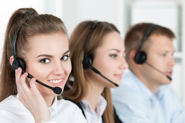 Portrait of call center worker accompanied by her team. Smiling customer support operator at work. Help and support concept