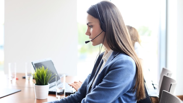 Portrait of call center worker accompanied by her team. Smiling customer support operator at work.