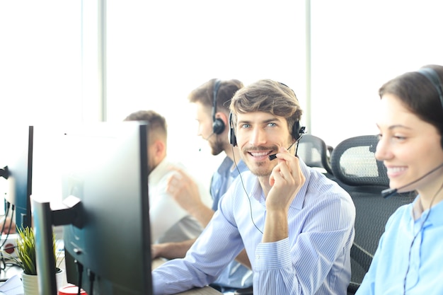 Portrait of call center worker accompanied by his team. Smiling customer support operator at work.