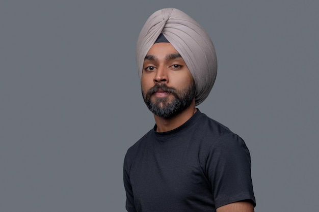 Portrait of a calm handsome middle-aged Indian man in a turban posing for the camera against the gray background