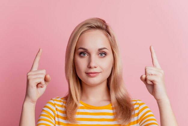 Portrait of calm positive girl direct fingers up empty space on pink background